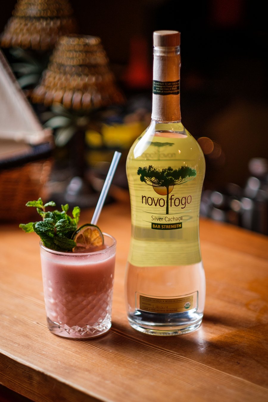 A Novo Fogo Bar Strength Silver Cachaca bottle sitting next to a pink cocktail!