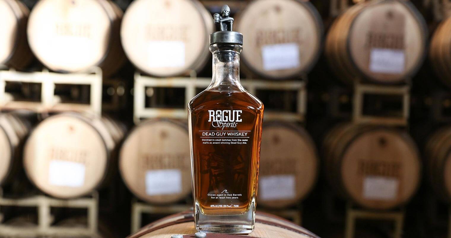 Rogue Ales distiller, whiskey bottle on barrel, barrel room background, featured image