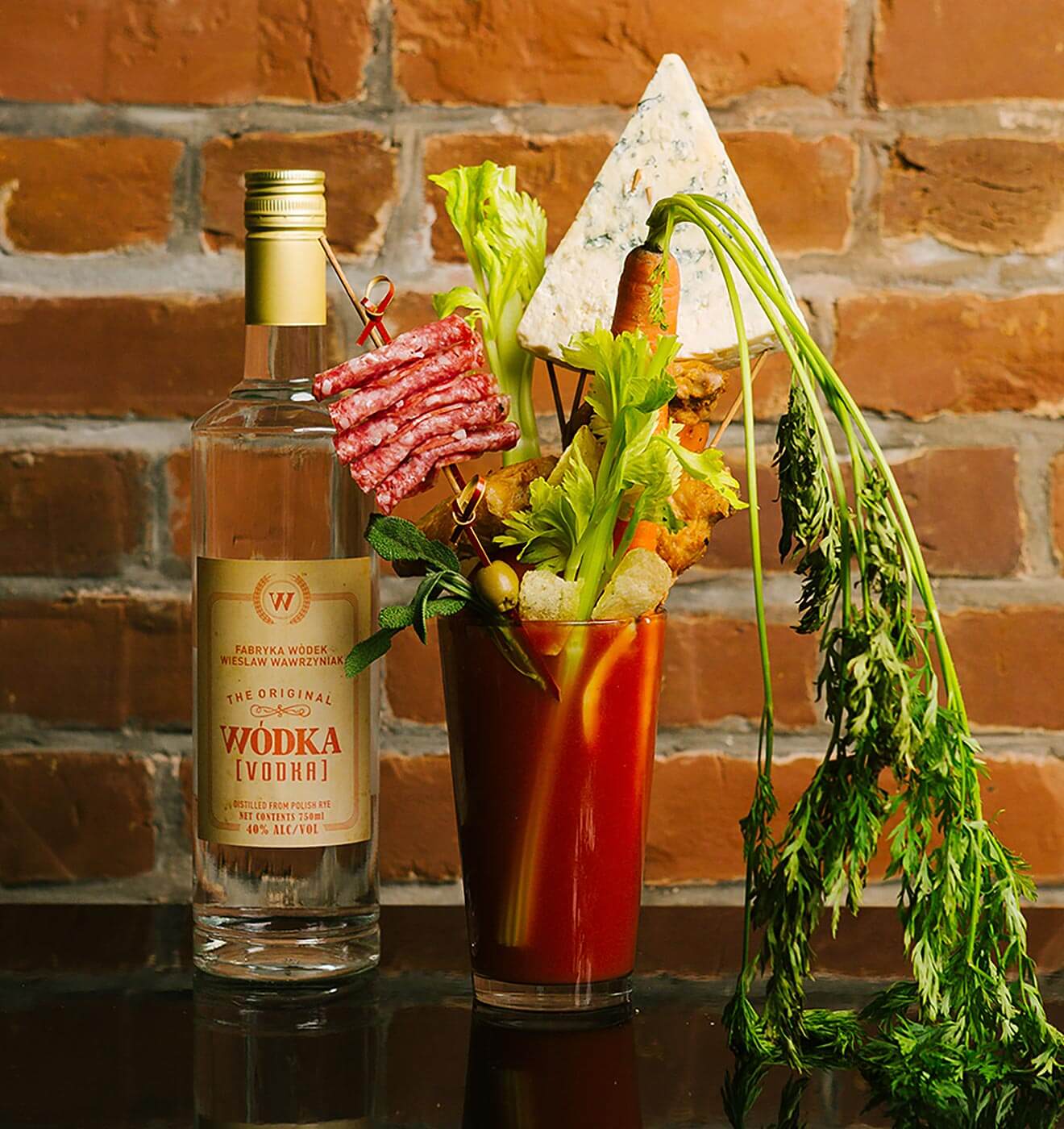 Wódka Bloody Mary, bottle and lots of garnish, brick wall background