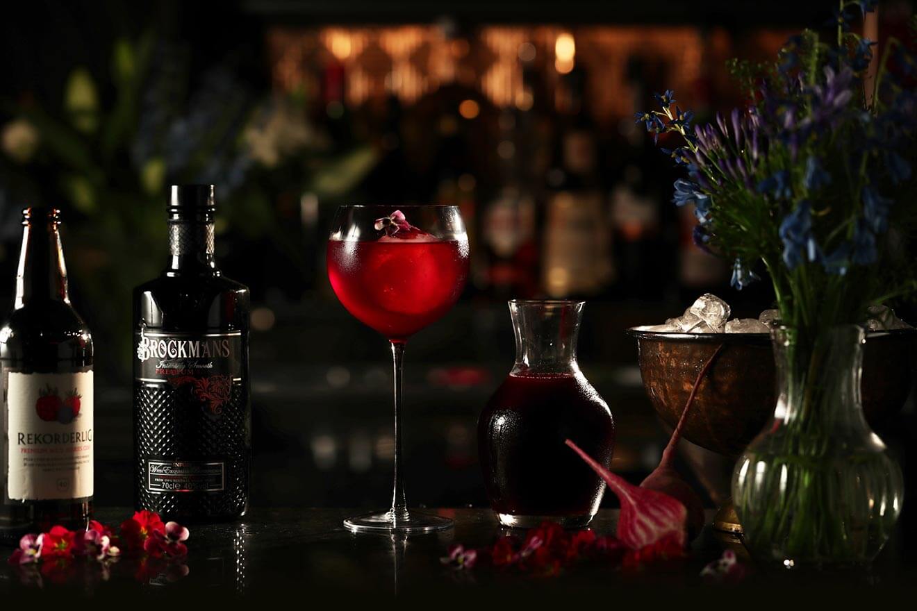 Brockmans Purple Spring, with bottles, cocktail, garnishes on dark