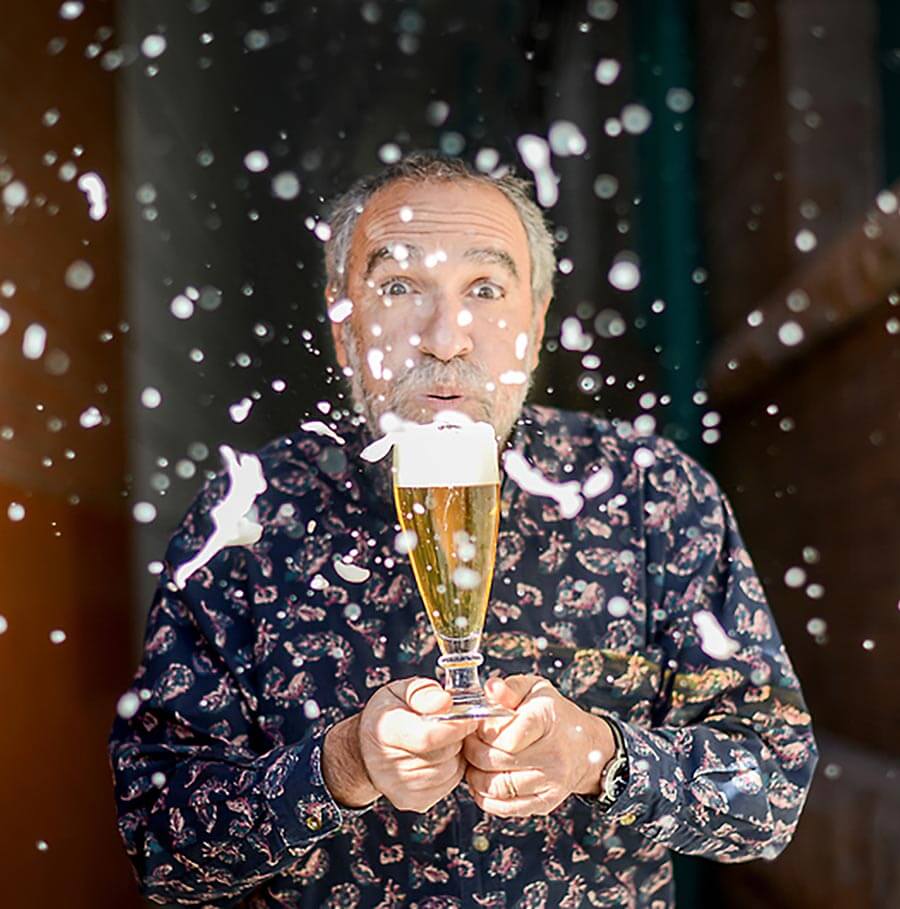 Charlie Papazian, blowing foam off the top of a beer