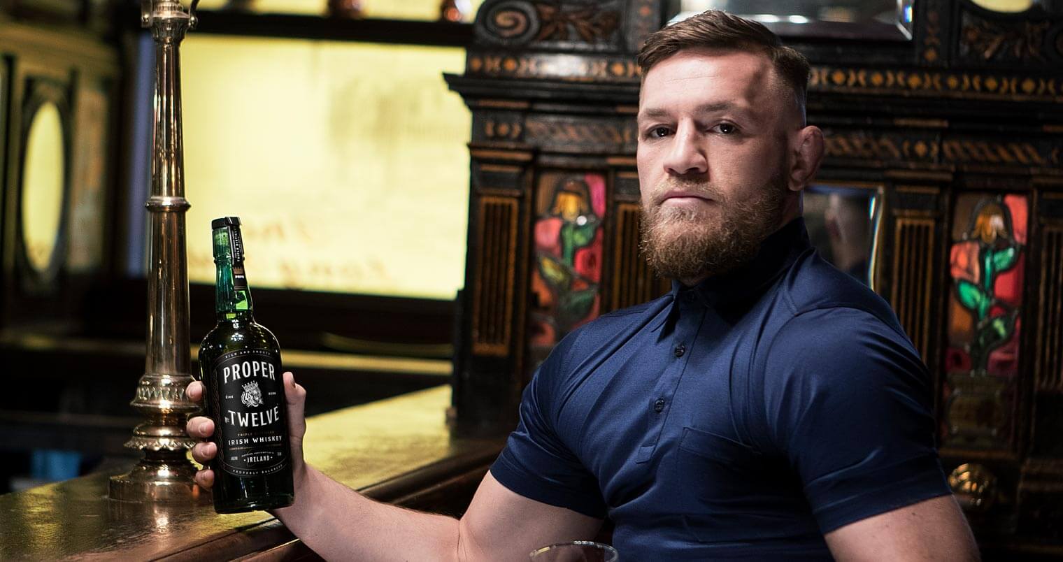 Connor McGregor's Irish Whiskey, holding bottle at bar, featured image