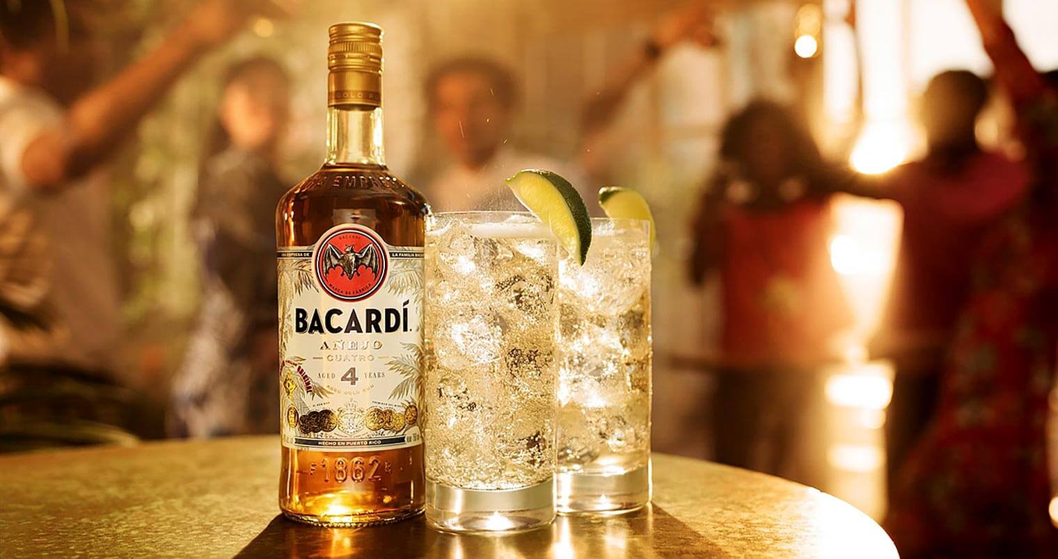 BACARDÍ Cuatro mismo, bottle and cocktails, people dancing in back, featured image