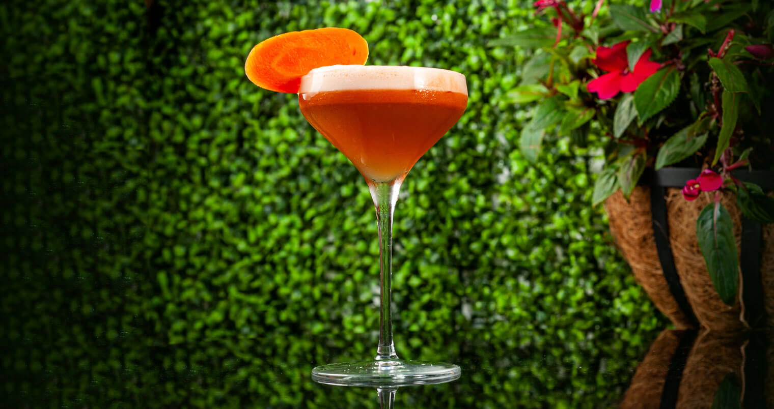 El Conejo Bueno, cocktail in garden with carrot garnish, featured image