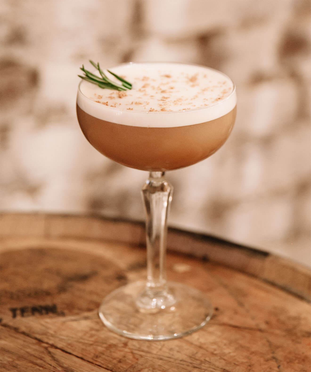 Creamy coffee cocktail garnished with rosemary on rustic background