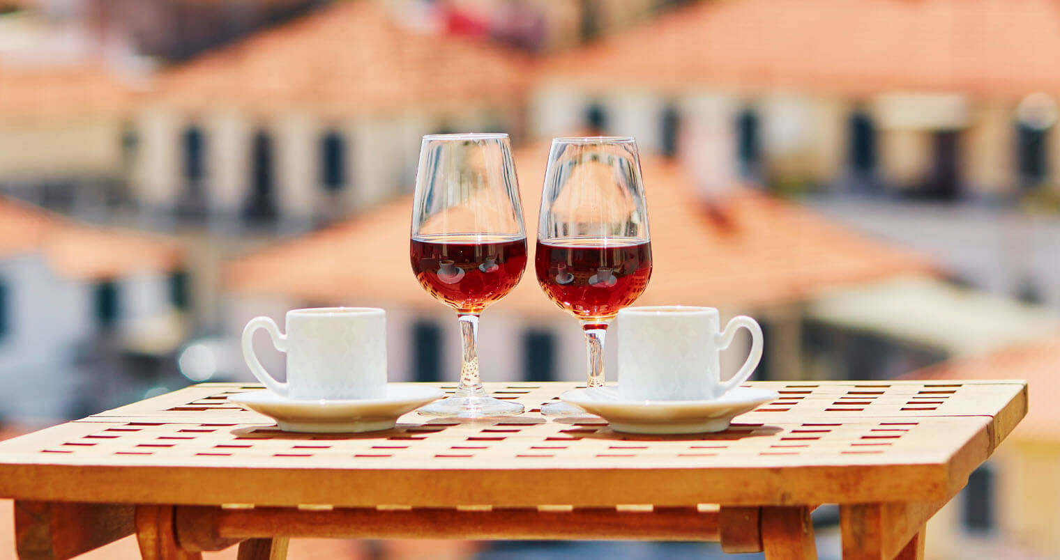 Two glasses of Madeira wine and two cups of fresh espresso coffee in cafe with view to Funchal town, Madeira, Portugal