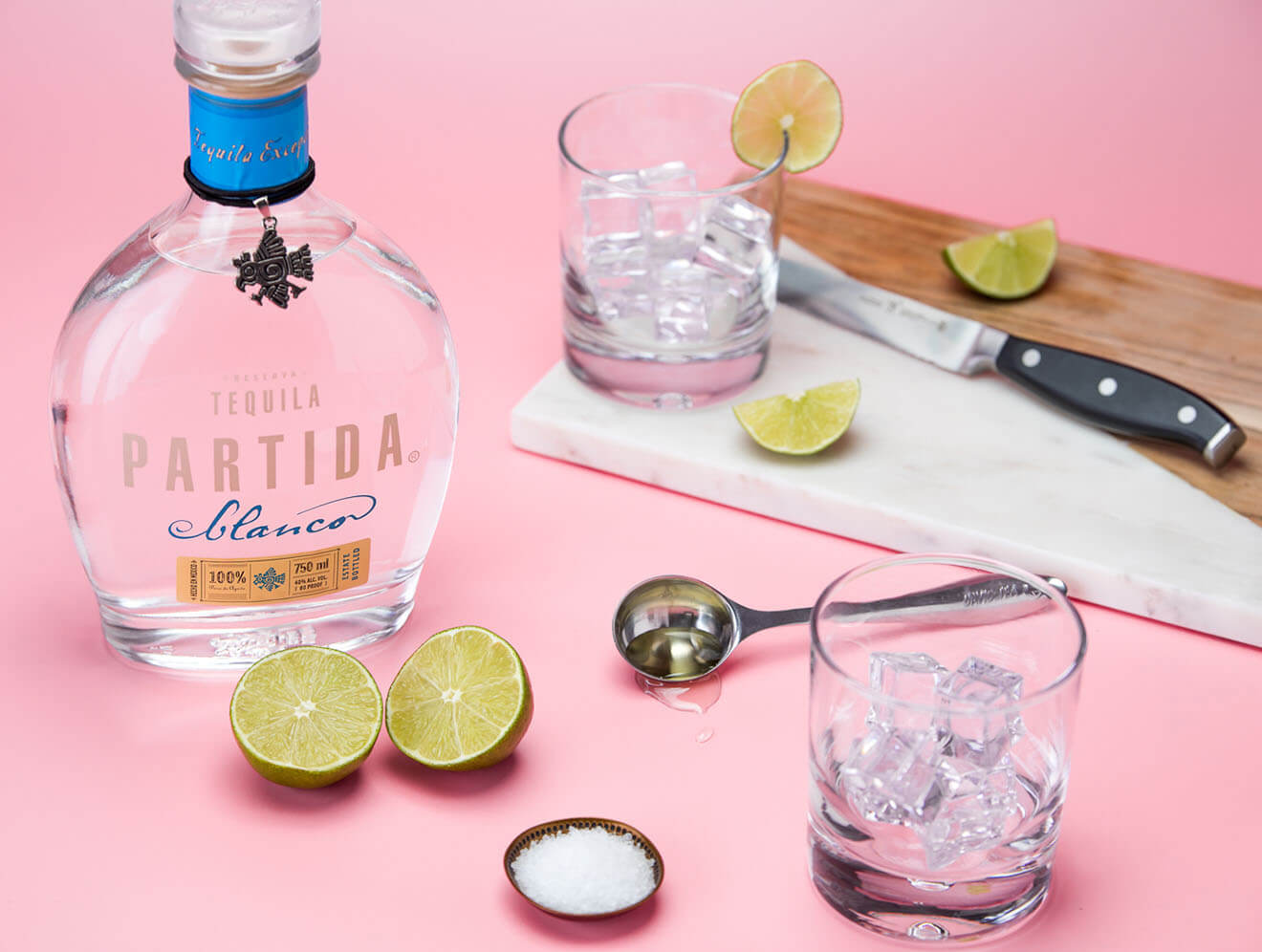 Partida Tequila, bottle, garnishes and bar tools, pink background