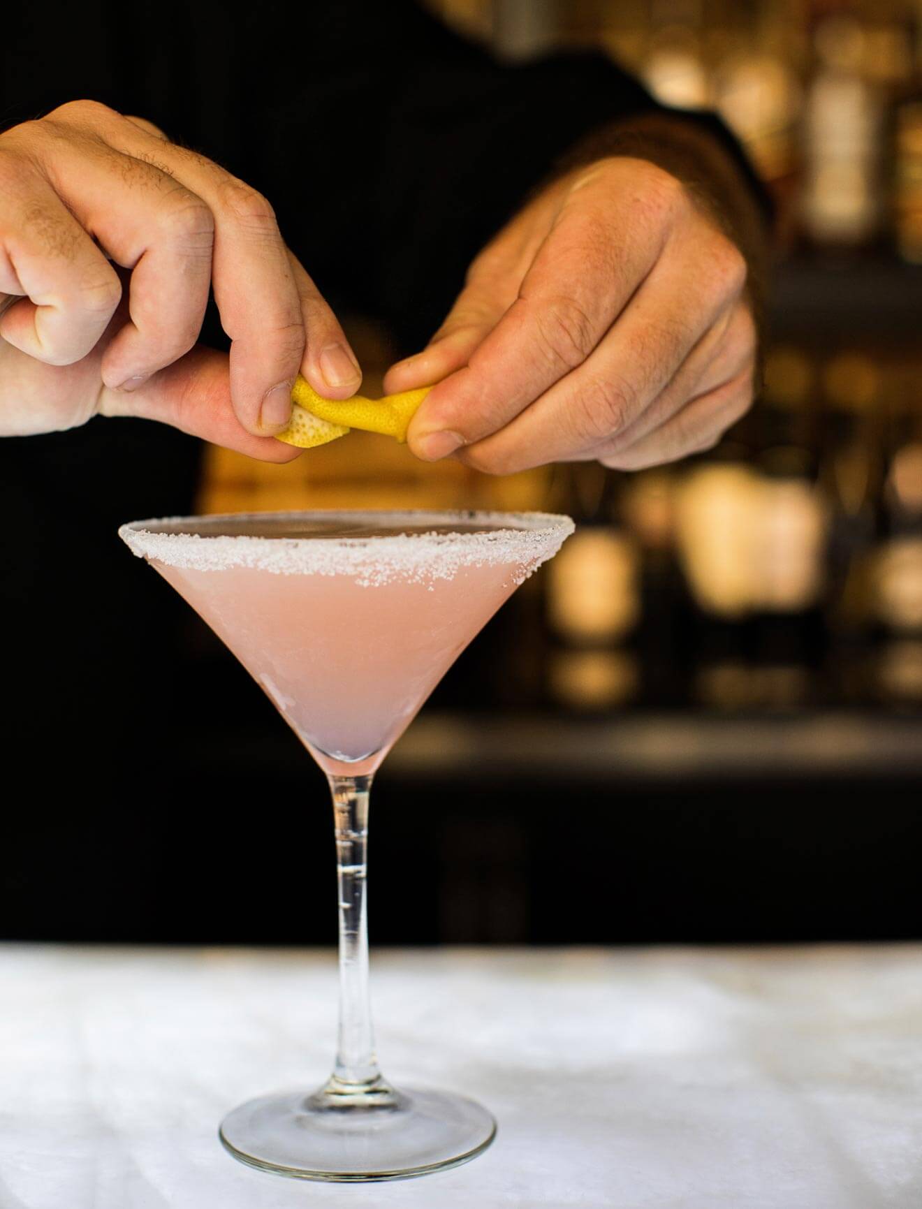 Bartender squeezing lemon onto martini