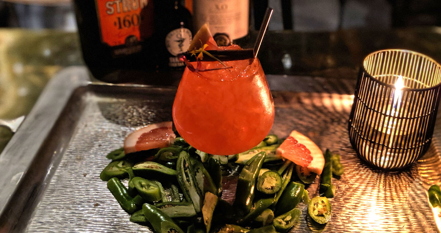 The Captain's Bride cocktail with pepper garnishes, and bottles in background, featured image