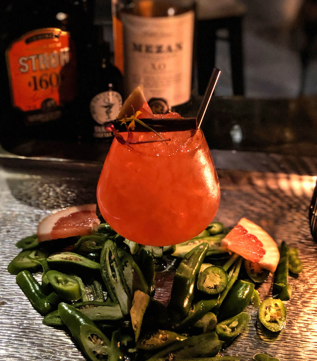 The Captain's Bride cocktail with pepper garnishes, and bottles in background