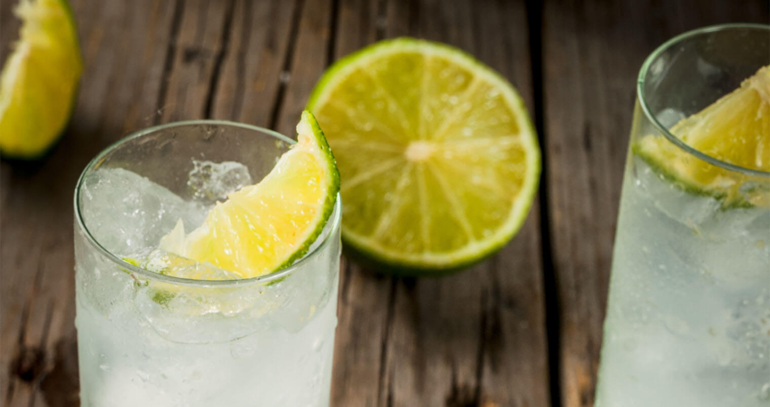 Alcoholic drink. Vodka and tonic highball cocktail with a lime garnish, on an old wooden rustic table., featured image