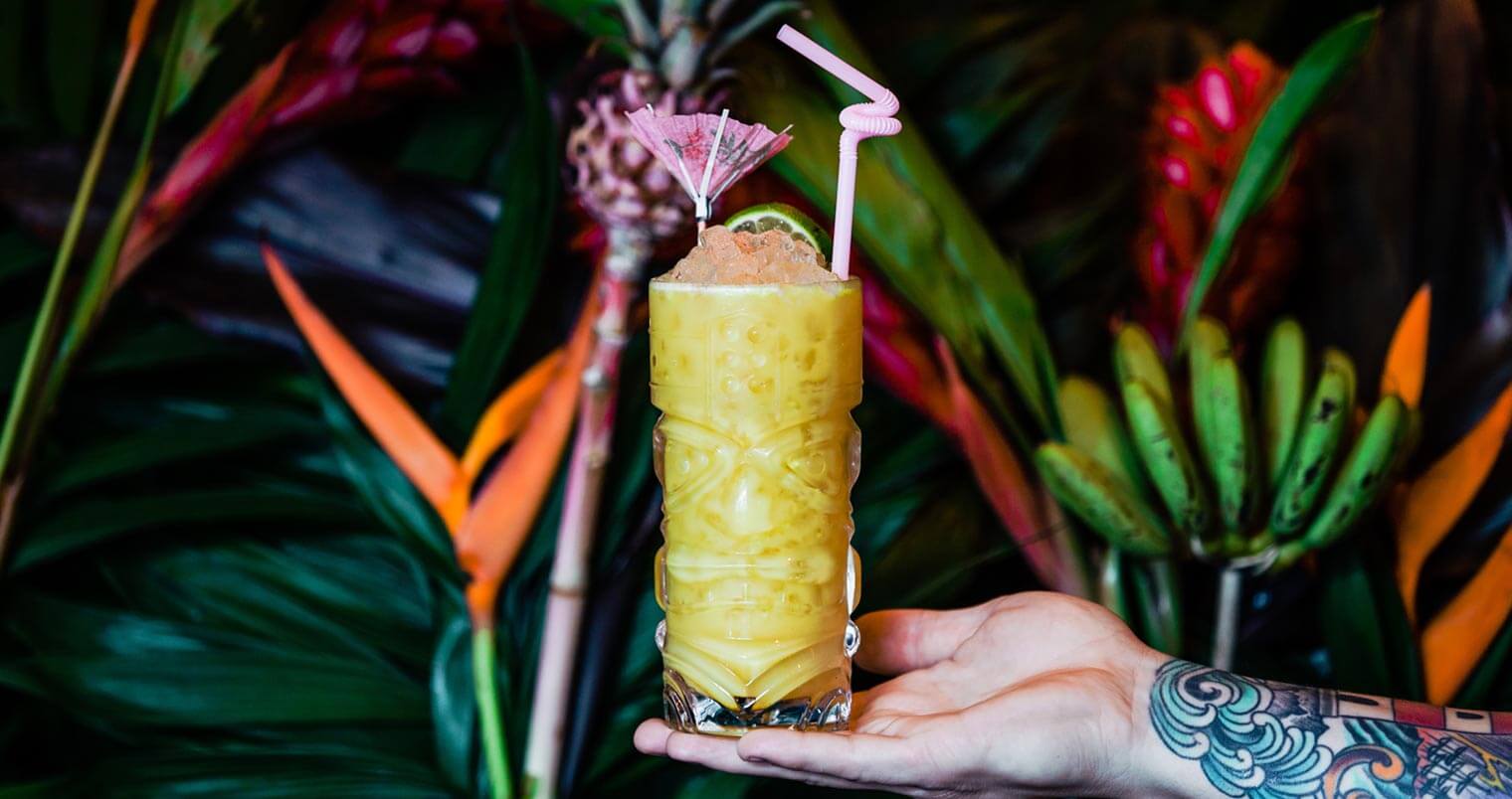 Yellowbelly cocktail in bartender's hand, tropical background, featured image