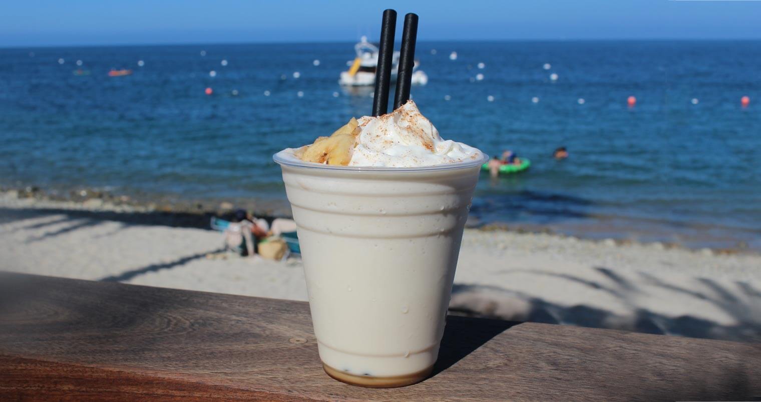 Buffalo Milk Cocktail, plastic cup and straws, beach background, featured image