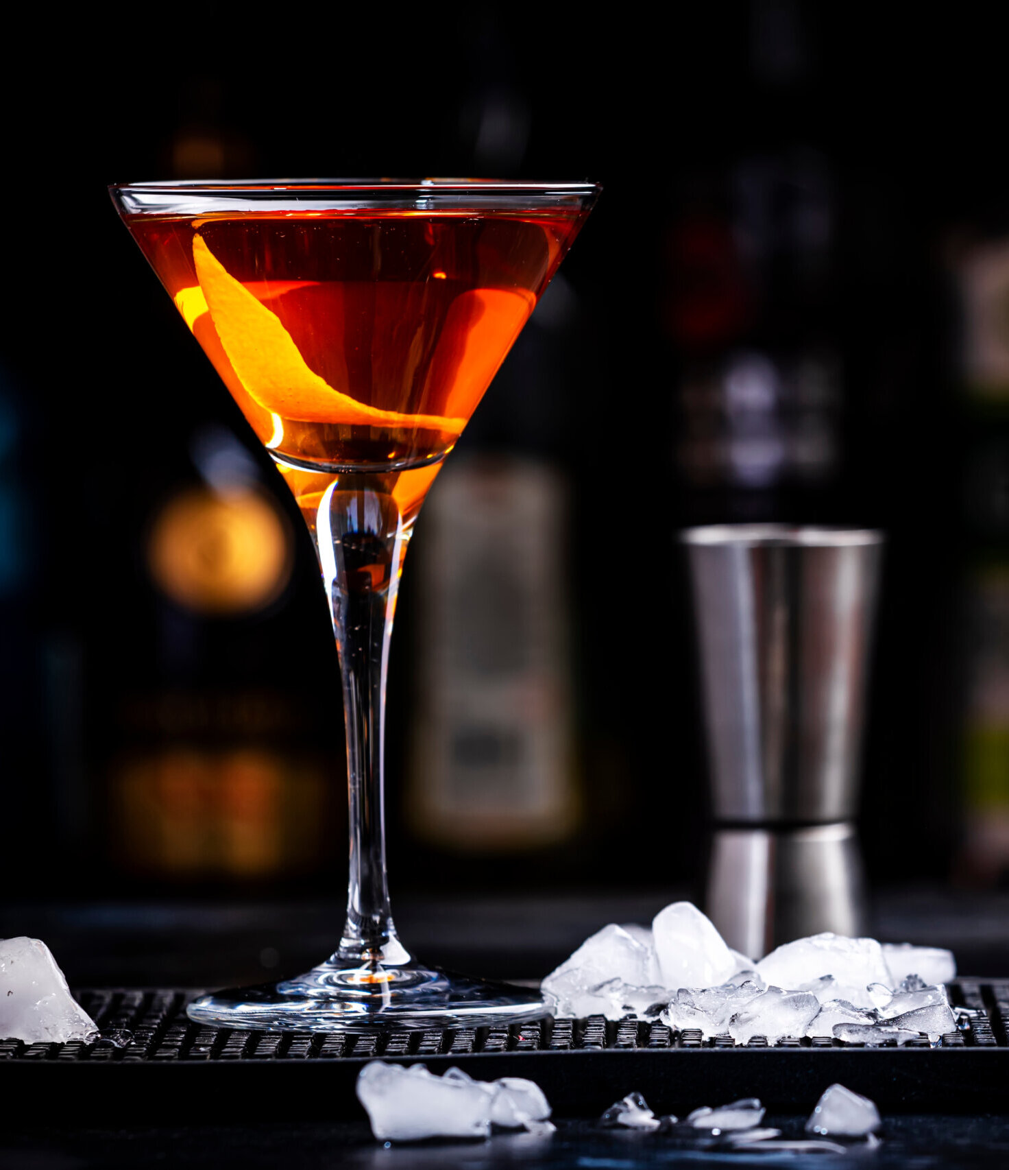 Orange alcoholic hard cocktail drink with scotch whiskey, vermouth and liquor in martini glass, dark bar counter background